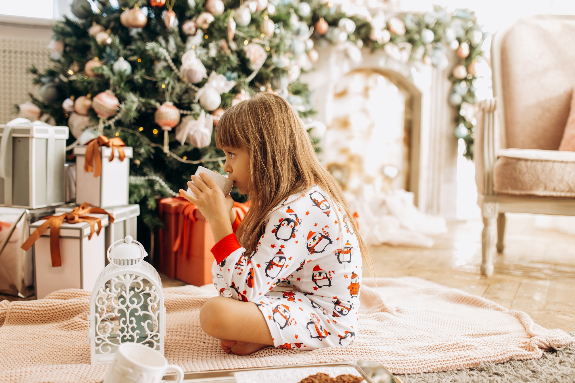 Little girl dressed in pajama sits o the carpet and drinks a co